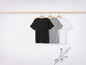 Des t-shirts noirs, gris et blancs sur un cintre en bois.