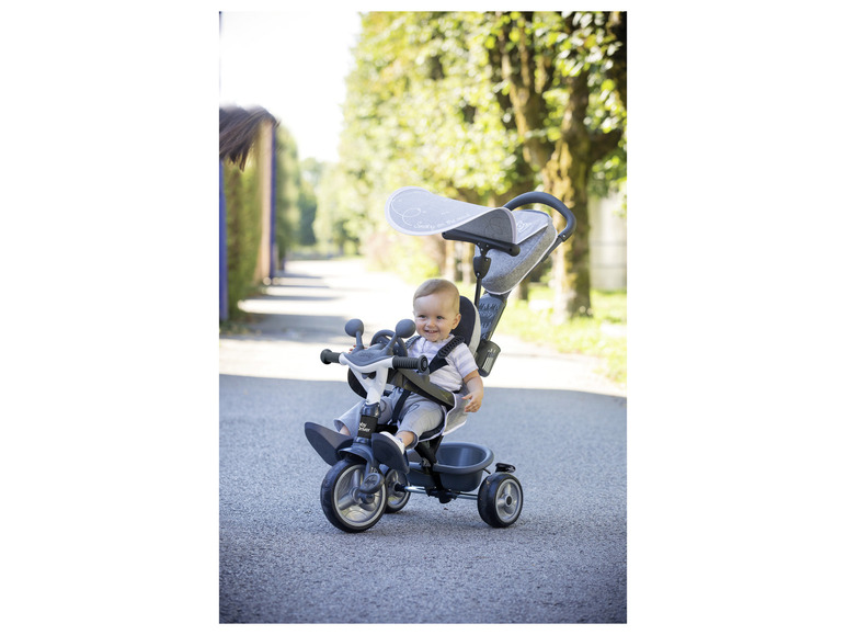 Un enfant roule sur un tricycle gris Smoby Baby Driver.
