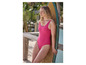 Une femme en maillot de bain rose s'appuie contre une planche de surf sur la plage.