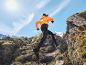 Un athlète court dans les montagnes avec un pantalon noir et une veste orange.