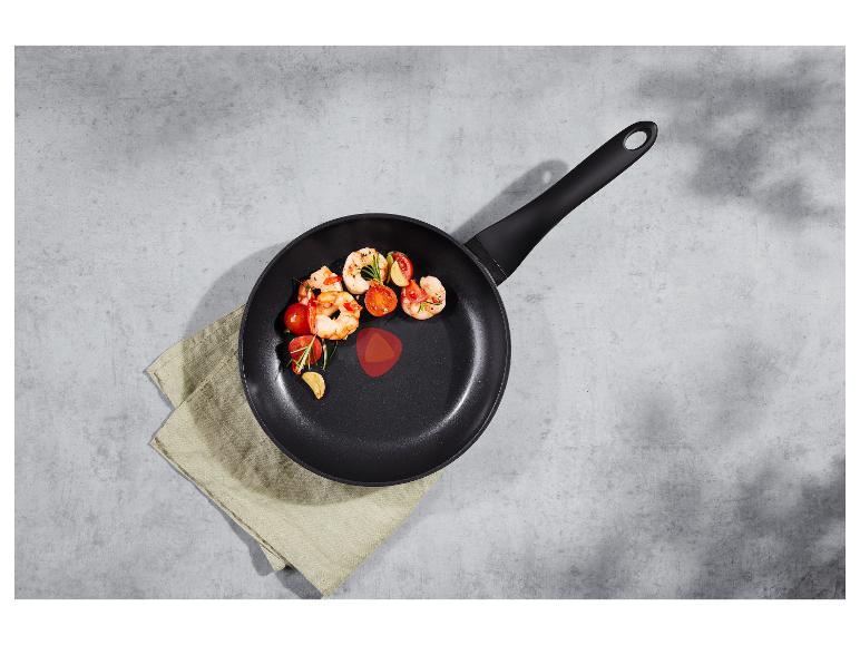 Poêle noire avec crevettes cuites, tomates cerises, ail et romarin sur une surface grise.