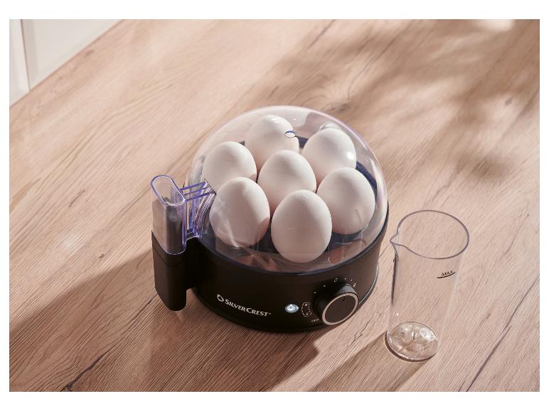 Cuiseur à œufs SilverCrest avec sept œufs et un verre doseur sur une surface en bois.