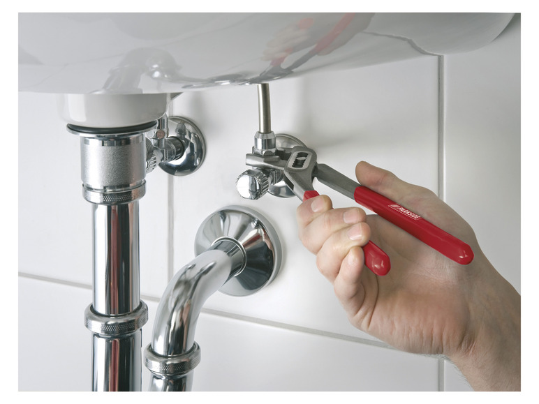 Un plombier répare un drain de lavabo avec une pince rouge Parkside.