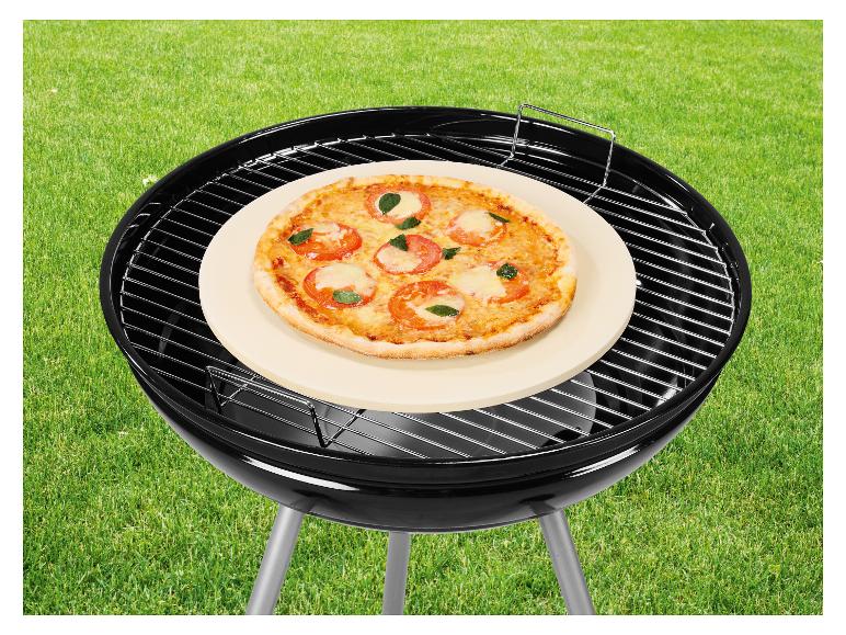 Pizza sur pierre à pizza sur barbecue au charbon de bois sur pelouse.