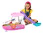 Une fille souriante joue avec un bateau jouet Barbie rose, avec toboggan et accessoires.