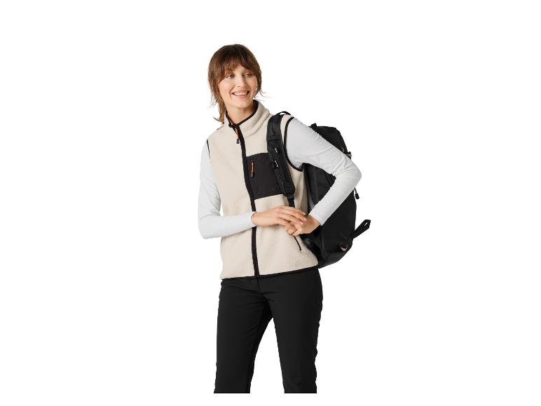 Femme en gilet polaire crème et pantalon noir, portant un sac à dos noir.