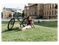 Une femme assise à côté d'un vélo électrique Gazelle vert dans un parc.