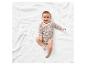 Un bébé souriant allongé sur une couverture blanche en tricot.