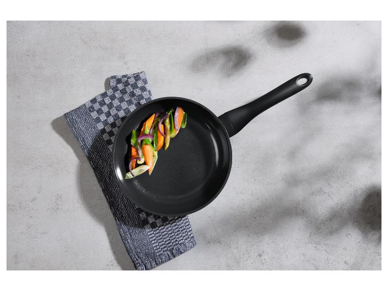Poêle avec légumes coupés sur un torchon à carreaux sur une surface en ciment.