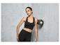 Une femme en brassière de sport et leggings s'appuie contre un mur avec un rouleau en mousse.