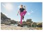 Femme en t-shirt noir et legging fuchsia faisant de l'exercice sur une plage rocheuse.