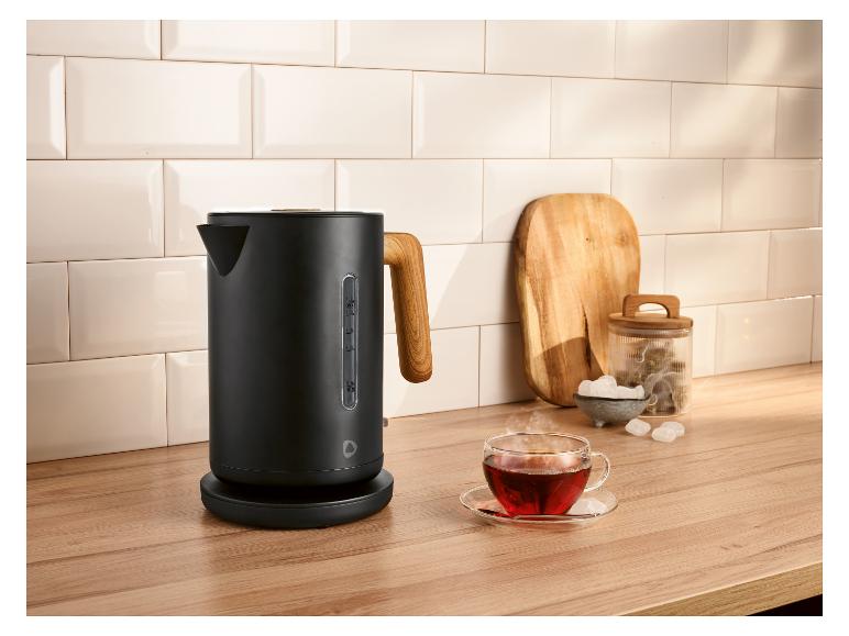 Bouilloire noire avec poignée en bois sur un comptoir de cuisine avec une tasse de thé.