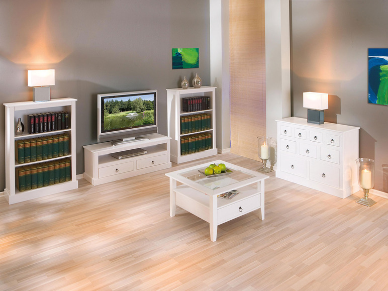 Bibliothèques blanches, meuble TV, table basse et commode à tiroirs dans un salon clair.