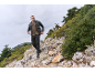 Homme en doudoune et pantalon cargo randonnant sur un sentier rocheux.