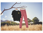 Un t-shirt noir avec un soleil et un pantalon rose accrochés à une branche.