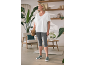 Femme en T-shirt blanc et legging capri gris, tenant un sac tressé, dans une pièce chaleureuse.