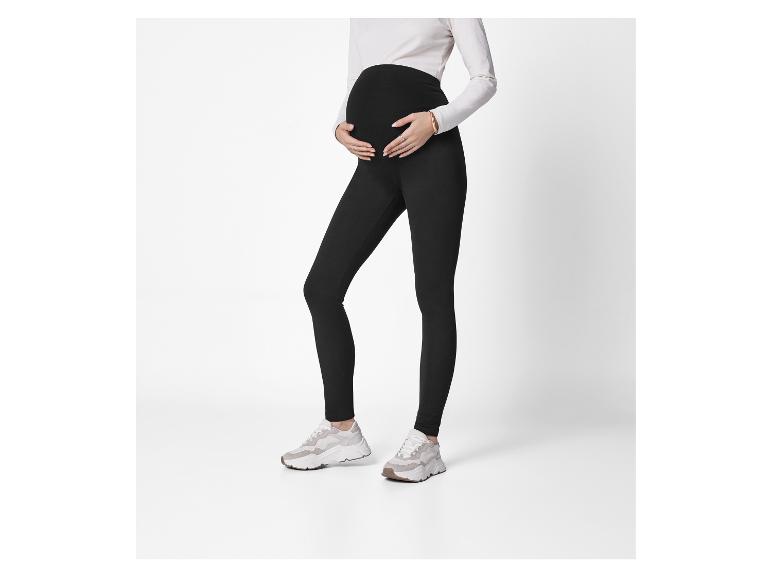 Femme enceinte portant des leggings noirs et un haut blanc, les mains sur le ventre.