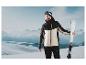 Un homme en veste et pantalon de ski tient des skis.