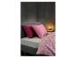 Lit avec oreillers roses et housse de couette à motif géométrique, à côté d'une table de chevet avec lampe.