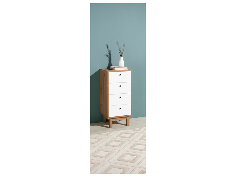 Une commode blanche à quatre tiroirs sur un tapis à motif géométrique.