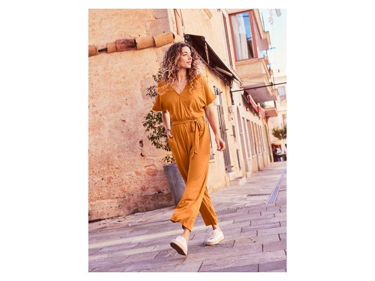 Une femme marche dans une rue avec une combinaison orange et des baskets blanches.