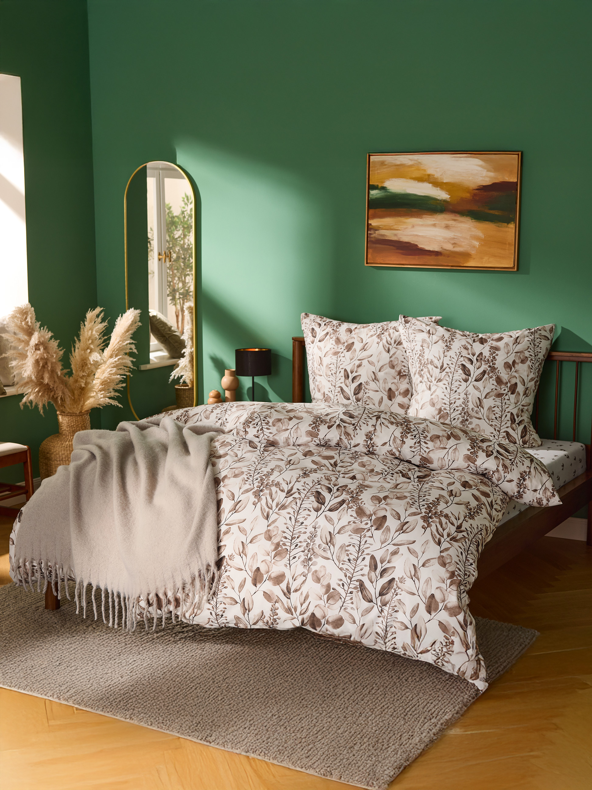 Chambre avec murs verts, lit avec parure de lit à motifs de feuilles et plaid beige.