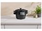 Casseroles empilées en fonte noire avec couvercles sur un comptoir blanc, avec herbes et épices en arrière-plan.