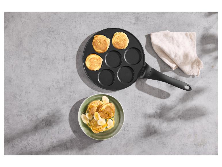 Poêle à crêpes avec des crêpes prêtes et une assiette de crêpes et de bananes.