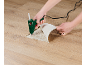 Mains utilisant un pistolet à colle chaude pour réparer une section soulevée de parquet stratifié.