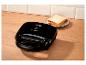 Appareil à croque-monsieur noir avec deux tranches de pain sur une assiette sur une surface en bois.