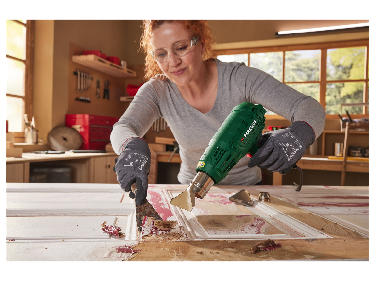 Une femme utilise un décapeur thermique Parkside pour enlever de la peinture d'une porte.