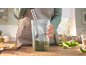 Préparation d'une sauce verte avec un mixeur plongeant dans un verre doseur sur une table en bois.