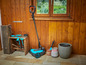 Une tondeuse robot Gardena bleue, des outils de jardinage et un pot de fleurs.