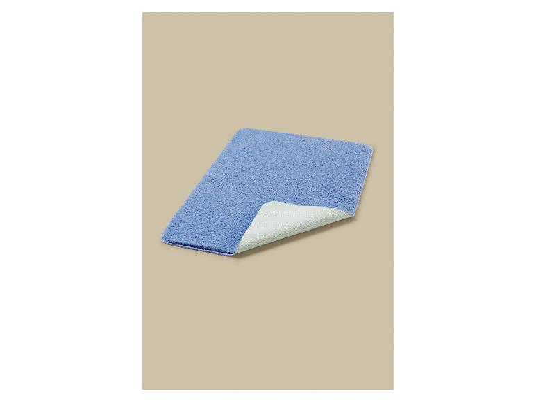 Un tapis de bain bleu rectangulaire avec un envers antidérapant blanc, partiellement plié.