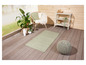 Un tapis vert à motif losange sur une terrasse en bois avec un pouf en tricot gris.