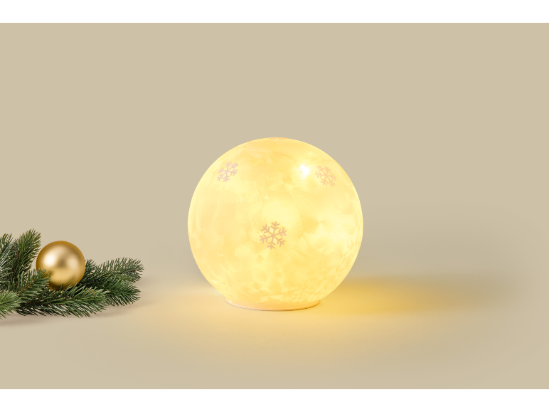 Lampe de Noël sphérique lumineuse avec motifs de flocons de neige à côté d'une branche de sapin