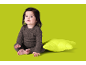 Bébé en grenouillère marron assis à côté d'un coussin vert.