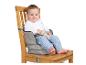 Bébé souriant assis dans un rehausseur en tissu gris sur une chaise en bois.