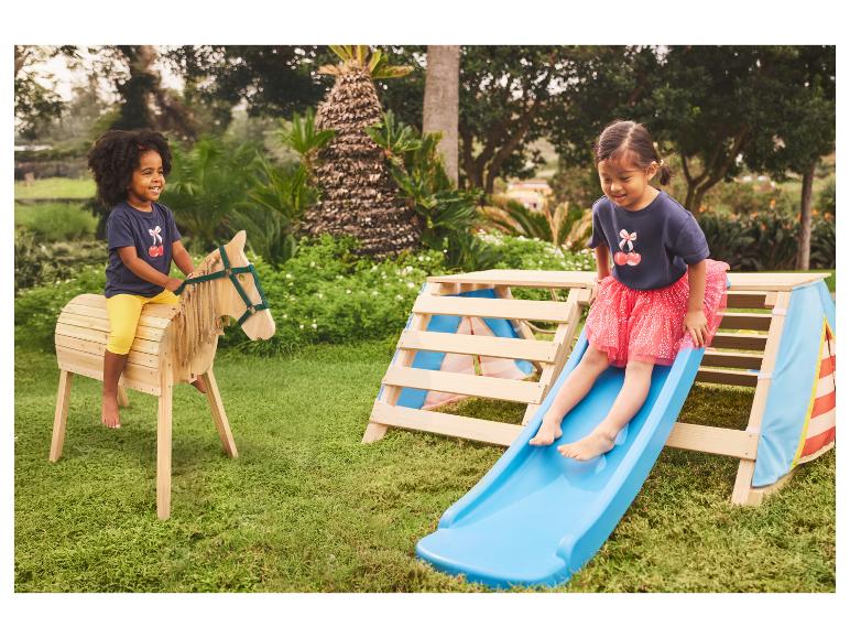 Deux enfants jouent dehors avec un cheval à bascule en bois et une structure de jeu en bois avec toboggan.