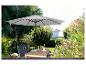 Parasol gris et table de jardin en bois avec chaises dans un jardin verdoyant.