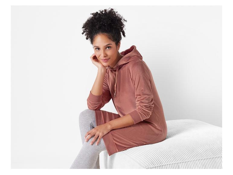 Une femme porte une robe à capuche rose avec des leggings gris.