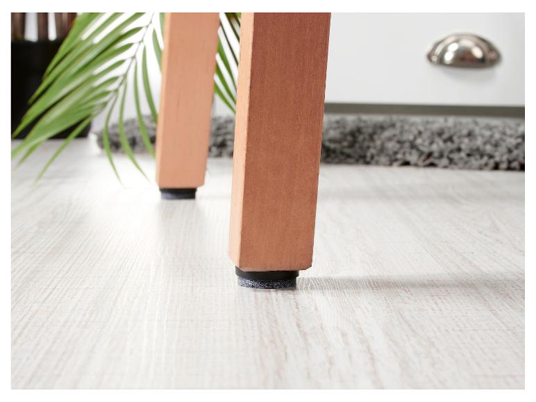 Pieds de meubles avec patins en feutre sur sol clair, avec plante et tapis en arrière-plan.