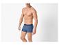 Homme torse nu en boxers bleus, posant sur fond blanc.