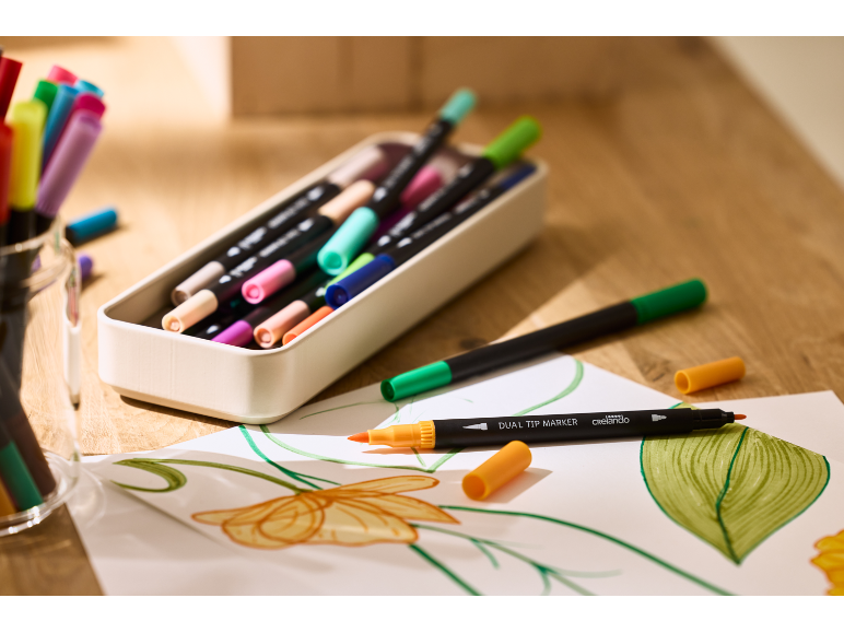 Marqueurs double pointe colorés et dessins sur une table en bois.