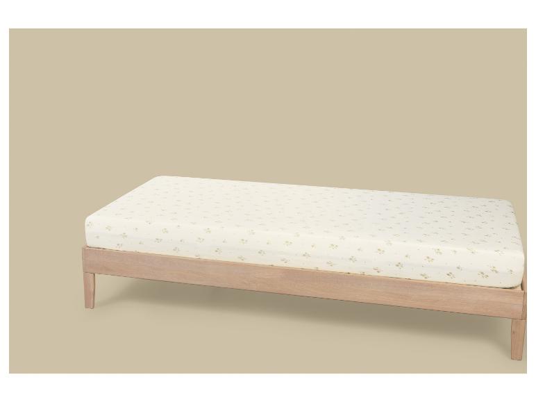 Lit simple en bois clair avec un matelas à motif floral sur fond beige.