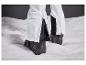 Pantalon de ski blanc avec des inserts noirs et des chaussures de ski noires dans la neige.