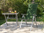 Une chaise pliante verte et une table avec un plateau en verre dans un jardin.