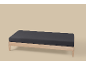 Un cadre de lit en bois avec un matelas gris foncé sur un fond beige clair.