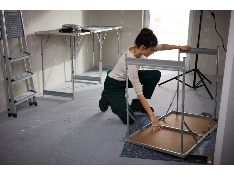 Femme assemblant une table de travail pliable dans un espace de construction.