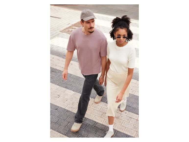 Un homme et une femme marchent dans la rue, il porte un t-shirt rose et une casquette, elle un pull blanc et une jupe.